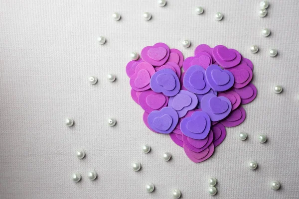 Cuori e perle viola adagiati su un tessuto beige — Foto Stock