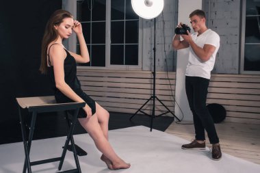 Bir erkek fotoğrafçı, beyaz arka planda bir kız modelin fotoğraflarını çekiyor.