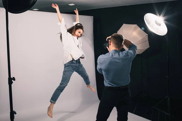 Bir erkek fotoğrafçı, beyaz arka planda bir kız modelin fotoğraflarını çekiyor.