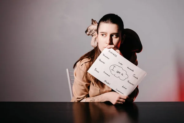 The girl teaching English and shows phrases using signs at with a cat. Innovative pedagogy to teaching in online school.A new english course is available online.