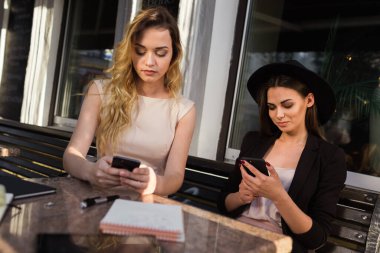 Şirin kız arkadaşlar kafenin verandasında oturan aletleri kullanırlar.