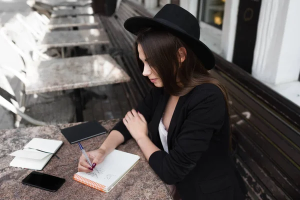 A young girl writer writes articles for a fashion magazine on a summer verand