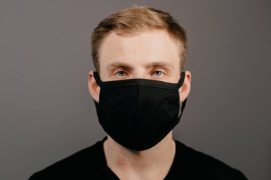 Siyah tişörtlü yakışıklı adam siyah tıbbi maske takıyor, gri arkaplan. Coronavirus covid-19 karantina dönemi konsepti
