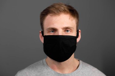 Siyah tişörtlü yakışıklı adam siyah tıbbi maske takıyor, gri arkaplan. Coronavirus covid-19 karantina dönemi konsepti