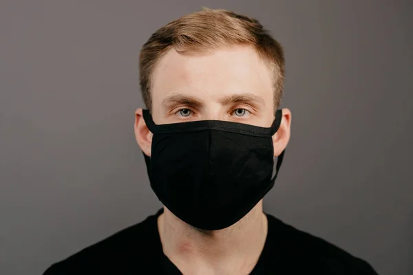 Siyah tişörtlü yakışıklı adam siyah tıbbi maske takıyor, gri arkaplan. Coronavirus covid-19 karantina dönemi konsepti