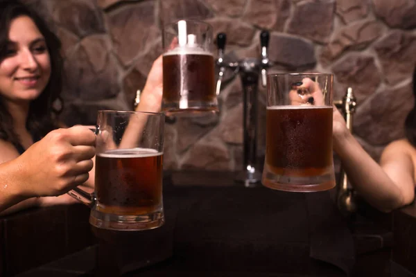 Mujeres caucásicas jóvenes felices en albornoz se sientan al lado de la piscina en la sauna, bebiendo cerveza fría. Salud. — Foto de Stock