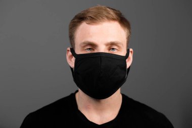Siyah tişörtlü yakışıklı adam siyah tıbbi maske takıyor, gri arkaplan. Coronavirus covid-19 karantina dönemi konsepti