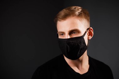 Siyah tişörtlü yakışıklı adam siyah tıbbi maske takıyor, gri arkaplan. Coronavirus covid-19 karantina dönemi konsepti