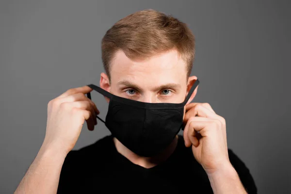 Siyah tişörtlü yakışıklı adam siyah tıbbi maske takıyor, gri arkaplan. Coronavirus covid-19 karantina dönemi konsepti