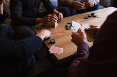 Birkaç adam bir kafede poker oynuyor, ellerinde kartlarla.