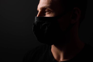 Siyah tişörtlü yakışıklı adam siyah tıbbi maske takıyor, gri arkaplan. Coronavirus covid-19 karantina dönemi konsepti