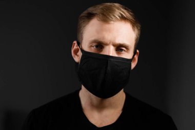 Siyah tişörtlü yakışıklı adam siyah tıbbi maske takıyor, gri arkaplan. Coronavirus covid-19 karantina dönemi konsepti