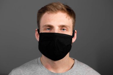 Siyah tişörtlü yakışıklı adam siyah tıbbi maske takıyor, gri arkaplan. Coronavirus covid-19 karantina dönemi konsepti