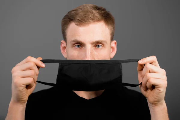 Siyah tişörtlü yakışıklı adam siyah tıbbi maske takıyor, gri arkaplan. Coronavirus covid-19 karantina dönemi konsepti