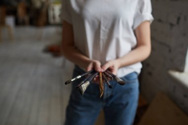 Genç bir sanatçı fırçalarıyla bir resim stüdyosunda duruyor..