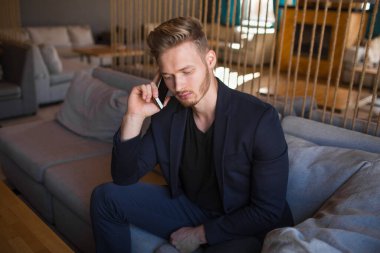 Sarışın, başarılı bir genç adam, modern bir nargile odasında telefonla konuşuyor.