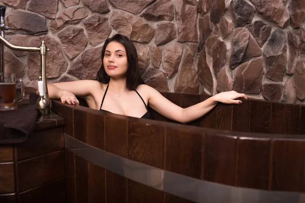 Piękna dziewczyna w stroju kąpielowym kąpiąca się w drewnianym jacuzzi w saunie. — Zdjęcie stockowe