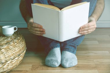 Kitap okurken kahve içme ahşap zemin üzerinde oturan genç adam.