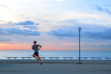 Güneş doğarken bir mesire plajın yanında çalışan tek bir adam. Bulutlar ve güneş ışığı. Boş kopya alanı