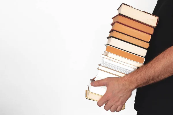Молодой человек держит стопку книг у белой стены . — стоковое фото