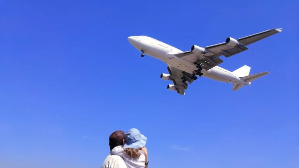 Homem e sua filha olhando para um avião pousando no céu. Conceito de reunião familiar. Espaço de cópia vazio — Fotografia de Stock