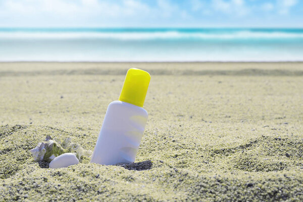 Sunscreen tube on the sand next to the beach. Empty copy space