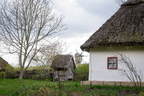 Ancient peasant Ukrainian house with a thatched roof, spring landscape in the old village of national architecture, Ukraine.