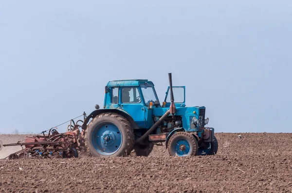 An old tractor in the field plows the land. Spring landscape of a countryside, a farm. — Stock Photo, Image