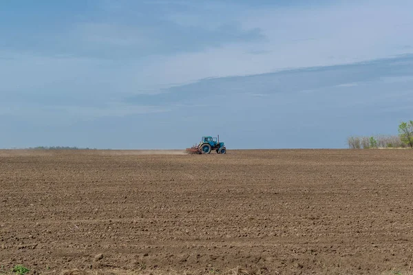 Un viejo tractor en el campo araña la tierra. Paisaje de primavera de un campo, una granja . — Foto de Stock