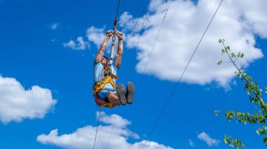 Ukrayna, Migea - 30 Haziran 2017: Zipline. Bir adam güzel bir mavi gökyüzü beyaz bulutlar ile karşı çelik kablo üzerinde kayar bir görüntü. Aşırı ve aktif dinlenme.
