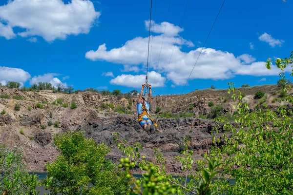 Ucrânia, Migea - 30 de junho de 2017: Zipline. Os homens no equipamento deslizam em um cabo de aço. Trolley Track Over the lake. Descanso extremo e ativo . — Fotografia de Stock