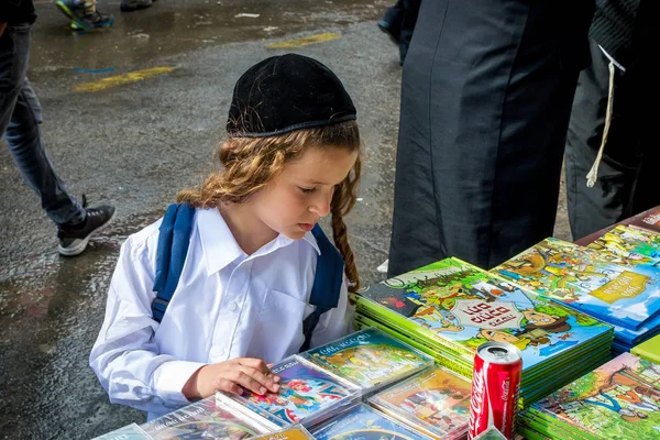 Uman, Ucrânia - 2 de outubro de 2016: Rosh Hashanah, Ano Novo Judaico 5777. Comércio de rua festivo. Uma criança Hasid com payos longos escolhe um livro . — Fotografia de Stock