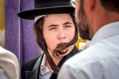 A young Hasid in a traditional Jewish hat and with long payos. Uman, Ukraine - 21 September 2017: Rosh Hashanah, Jewish New Year. clipart