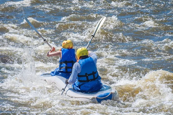 Rafting, kajakozás. Két sportolók sportfelszerelések vitorlázik a felfújható gumicsónak a forrásban lévő víz patak. Csapatmunka. Víz vízcseppek közelről. Extrém sport. — Stock Fotó