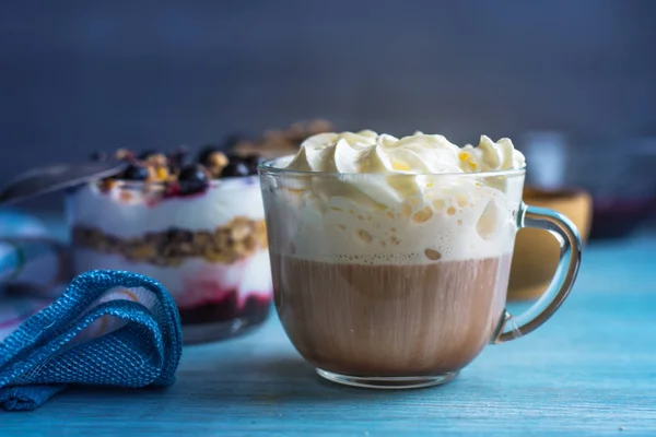 A cup of coffee with whipped cream and parfait for breakfast on a rustic wooden background close-up