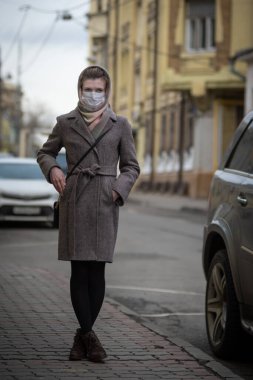 Koruyucu tıbbi maskeli çekici bir kadın bir arabanın yanında duruyor. Virüslere karşı koruma - grip, koronavirüs ve sis