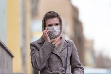 Grip virüslerine karşı tıbbi koruyucu maskeli çekici Avrupalı beyaz kadın ve Coronavirus COVID-19 şehrin caddesinde telefonla konuşuyor.