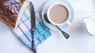 Kahvaltı - sütlü bir fincan kahve, süt sürahisi ve yeşil bir masada taze ekmek, üst manzara.