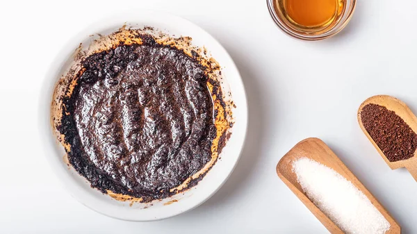 Homemade coffee body scrub made from coffee, sugar and butter in a bowl on a light background