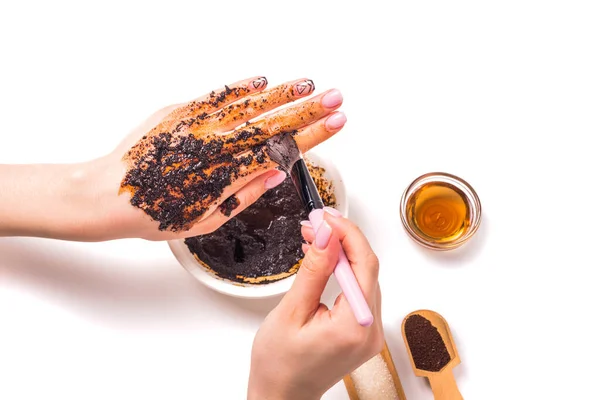 Woman puts a coffee scrub on her hands with a brush