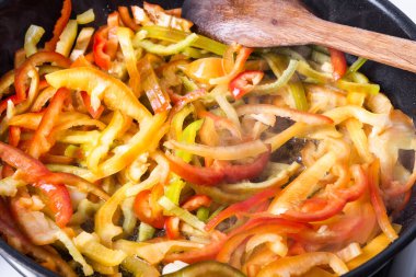 Dilimlenmiş tatlı biber tavada kızarır ve ahşap bir kaşıkla karıştırılır - pişirme sosu