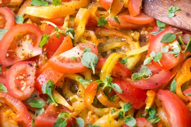 Dilimlenmiş domates ve fesleğen yapraklı dolma biber tavada kızartılır ve ahşap bir kaşıkla karıştırılır, yakın plan - pişirme sosu.