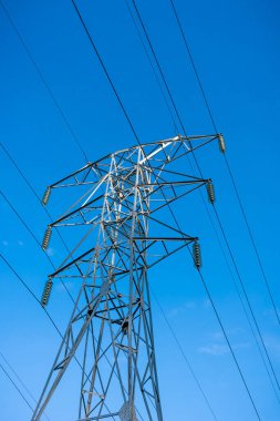 Yüksek voltajlı elektrik hattının yüksek kuleleri mavi gökyüzüne karşı, alt manzara