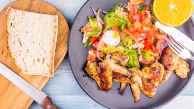 Lezzetli kızarmış tavuk kanatları, siyah tabakta sebze salatası ve bir parça ekmek.
