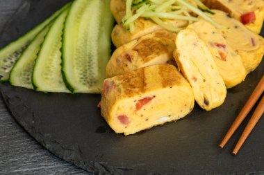 Geleneksel Japon omleti Tamagoyaki ve siyah tahta üzerinde salatalık dilimlenmiş yemek çubukları, yakın çekim
