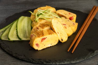 Geleneksel Japon omleti Tamagoyaki ve siyah tahta üzerinde salatalık dilimlenmiş yemek çubukları, yakın çekim