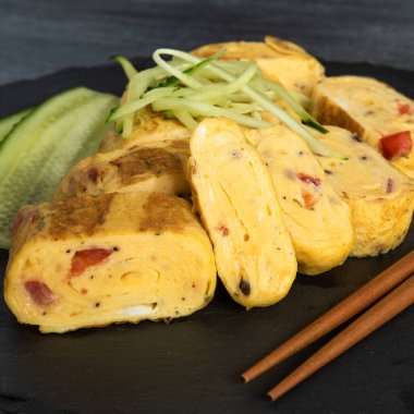Geleneksel Japon omleti Tamagoyaki ve siyah tahta üzerinde salatalık dilimlenmiş yemek çubukları, yakın çekim