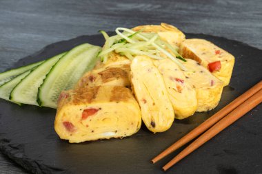Geleneksel Japon omleti Tamagoyaki ve siyah tahta üzerinde salatalık dilimlenmiş yemek çubukları, yakın çekim
