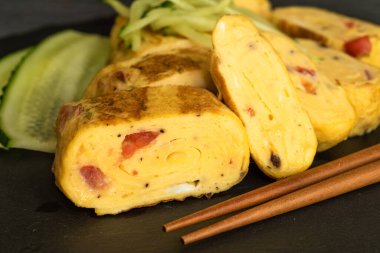 Geleneksel Japon omleti Tamagoyaki ve siyah tahta üzerinde salatalık dilimlenmiş yemek çubukları, yakın çekim