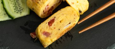 Geleneksel Japon omleti Tamagoyaki ve siyah tahta üzerinde salatalık dilimlenmiş yemek çubukları, yakın çekim